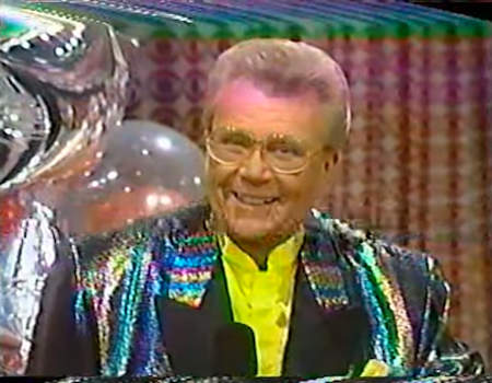 Rod is wearing an oil-slick-colored sequined jacket with black lapels and a yellow collarless silk shirt with matching pocket square