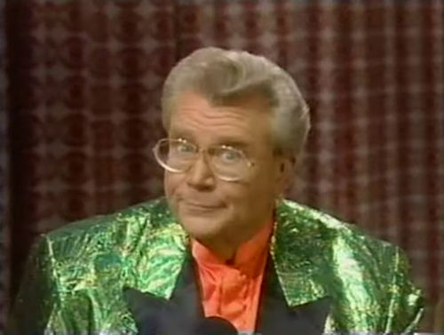 Rod is wearing a shiny green jacket with black lapels & salmon collarless silk shirt