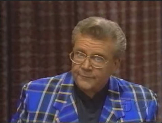 Rod is wearing a blue/black/white tartan jacket & black collarless silk shirt