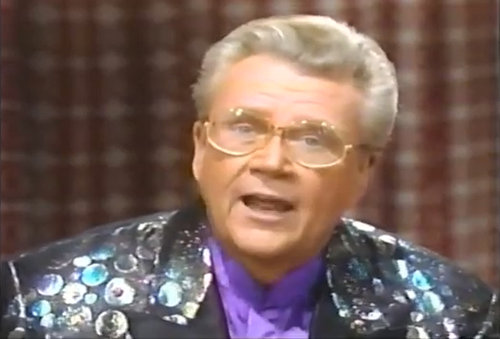 Rod is wearing a black jacket with shiny dots, black lapels & purple collarless silk shirt
