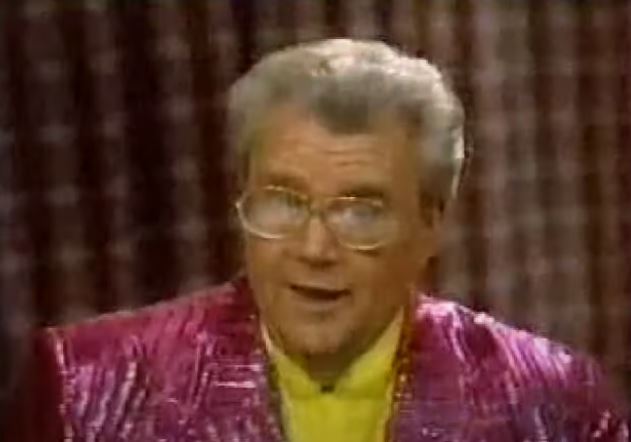 Rod is wearing a shiny purple/purple-striped jacket & yellow silk collarless shirt