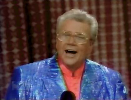 Rod is wearing a shiny blue/blue-striped jacket & salmon collarless silk shirt