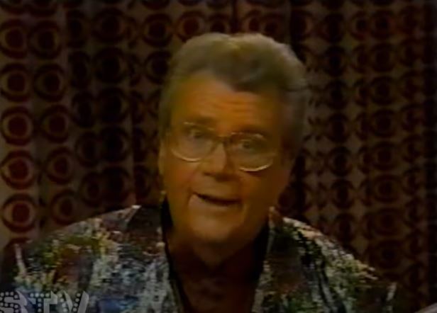 Rod is wearing a mottled shiny jacket & dark-red silk collarless shirt