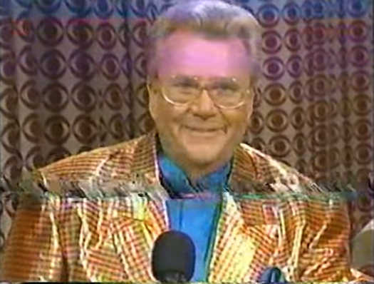 Rod is wearing a holographic orange-gingham jacket & blue collarless silk shirt with Matching pocket square
