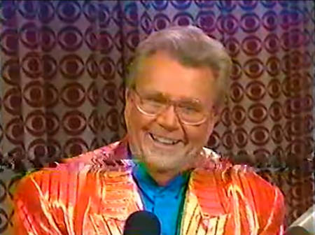 Rod is wearing a shiny orange/orange-striped jacket & blue collarless silk shirt