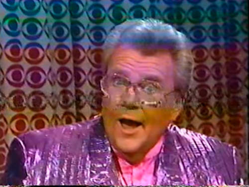 Rod is wearing a shiny purple/purple striped jacket & pink collarless silk shirt