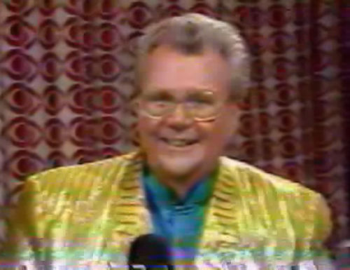 Rod is wearing a shiny yellow/yellow-striped jacket & teal blue collarless silk shirt