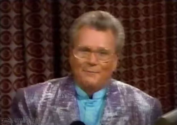 Rod is wearing a shiny silver/purple jacket & light-blue silk collarless shirt