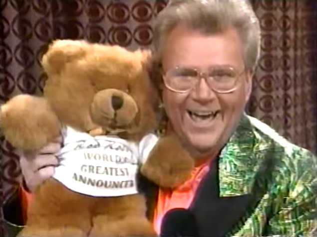 Rod is wearing a shiny green-patterned jacket with black lapels, salmon collarless silk shirt & is holding a teddy bear