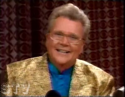Rod is wearing a gold jacket & blue collarless silk shirt