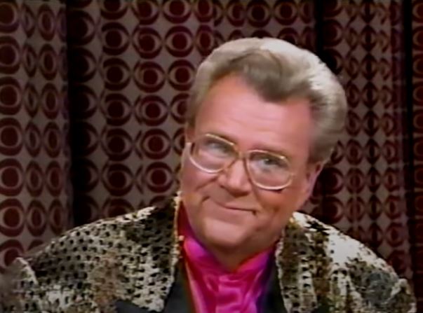 Rod is wearing a gold jacket w/ black dots & black lapels & pink silk collarless shirt