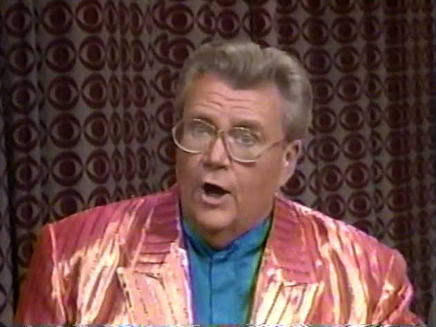 Rod is wearing a shiny salmon/red-striped jacket & blue collarless silk shirt