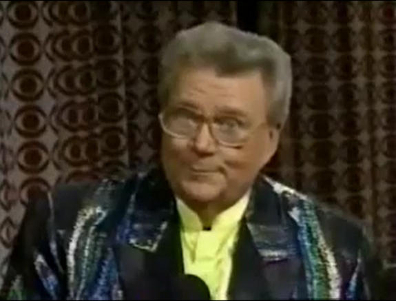 Rod is wearing a shiny 'oil-slick' jacket with black lapels & yellow collarless silk shirt