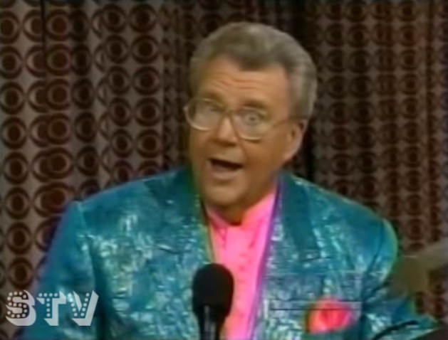 Rod is wearing a sparkly teal jacket & pink silk collarless shirt with matching handkerchief