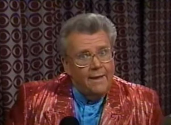 Rod is wearing a shiny red/red-striped jacket & blue collarless silk shirt