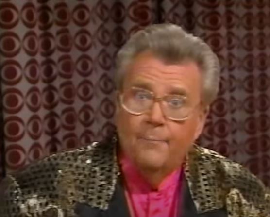 Rod is wearing a gold jacket with black spots and black lapels & pink silk collarless shirt