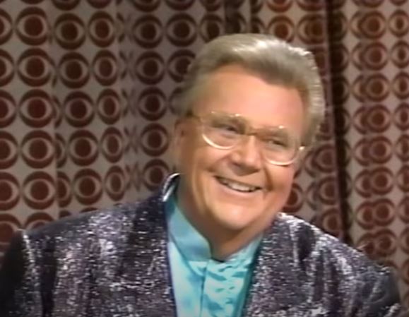 Rod is wearing a shiny silver jacket & light-blue collarless silk shirt