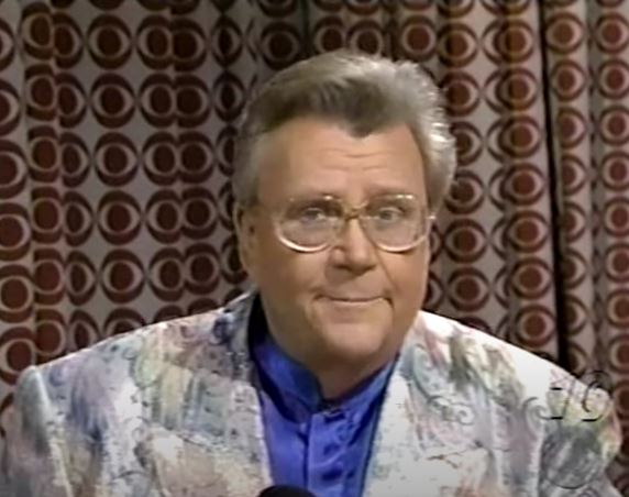 Rod is wearing a multi-pastel-patterned jacket & blue collarless silk shirt