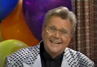 Rod is wearing a shiny silver jacket covered in black dots with white lapels & a black collarless silk shirt