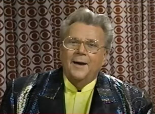 Rod is wearing a dark sequined jacket with black lapels & yellow collarless silk shirt