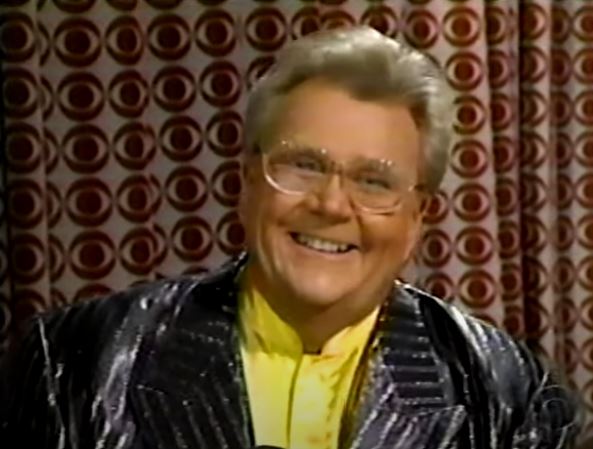 Rod is wearing a shiny Black/silver-striped jacket & yellow collarless silk shirt