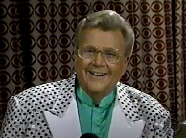 Rod is wearing a shiny silver jacket with black dots and white lapels & green collarless silk shirt