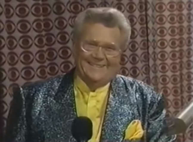 Rod is wearing a shiny green/gray jacket, yellow collarless silk shirt & matching pocket square