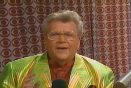 Rod is wearing a shiny light-green/gold striped jacket & brown collarless silk shirt with matching pocket square