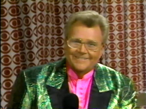 Rod is wearing a shiny green irredescent jacket with black lapels & pink collarless silk shirt