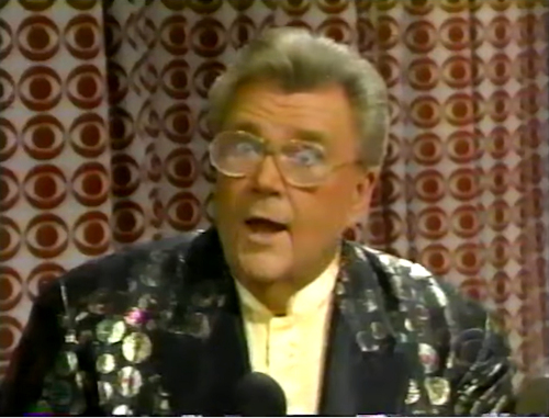 Rod is wearing a black jacket with gold circles/dots, black lapels & light-yellow collarless silk shirt