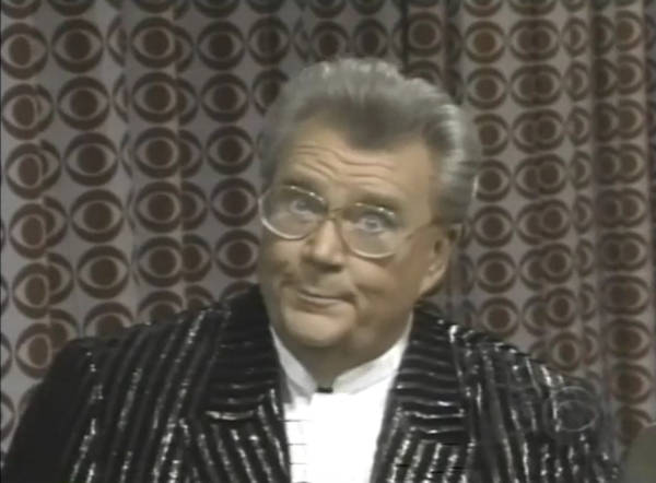 Rod is wearing a black & silver-striped jacket & white collarless silk shirt