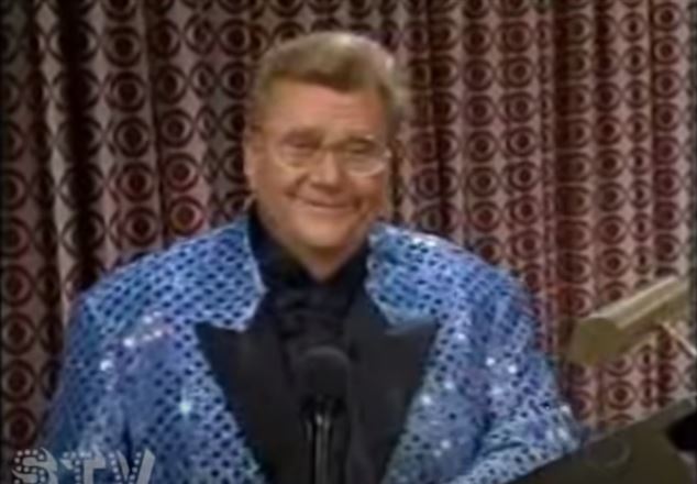 Rod is wearing a blue sequined jacket with black lapels & a black collarless silk shirt