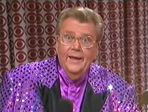 Rod is wearing a purple sequined jacket with shiny spots, black lapels & a purple collarless silk shirt