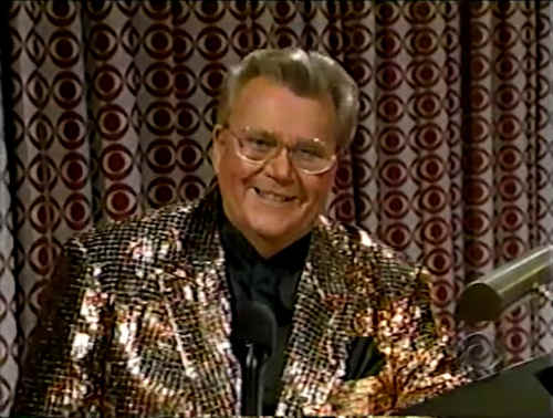 Rod is wearing a brown sequined jacket & black collarless silk shirt with matching pocket square