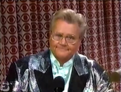 Rod is wearing a shiny silver jacket with black lapels & very light-blue collarless silk shirt