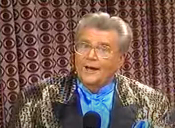 Rod is wearing a shiny gold jacket with black spots, black lapels & a blue collarless silk shirt with matching pocket square