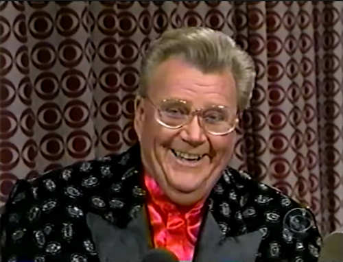 Rod is wearing a black jacket with silver circles & red collarless silk shirt