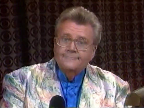 Rod is wearing a shiny holographic- paisley-patterned jacket & blue collarless silk shirt