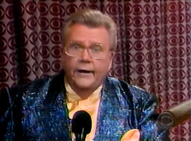 Rod is wearing a sparkly dark-blue jacket & mustard-colored pocket square & collarless silk shirt