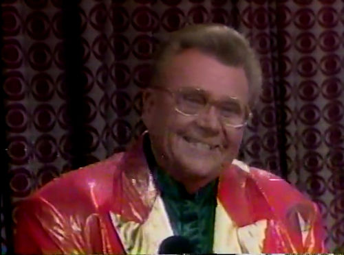 Rod is wearing a shiny red jacket with gold lapels & a dark-green collarless silk shirt