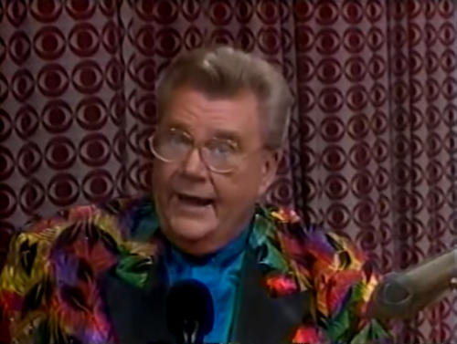 Rod is wearing a multi-colored feather-patterned jacket with black lapels & a blue collarless silk shirt