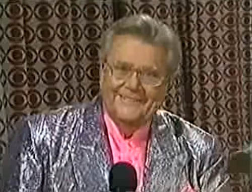 Rod is wearing a shiny silver jacket & pink collarless silk shirt with matching pocket square