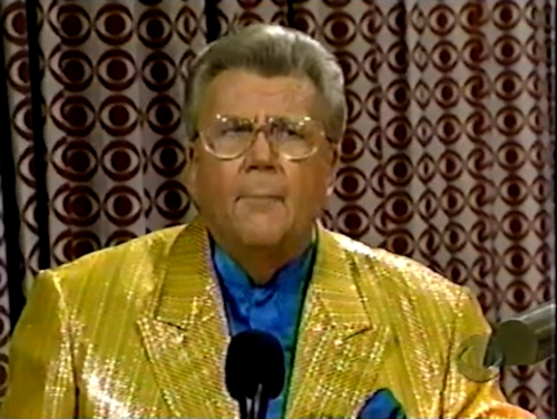 Rod is wearing a gold-striped sequined jacket & blue collarless silk shirt w/ matching pocket square