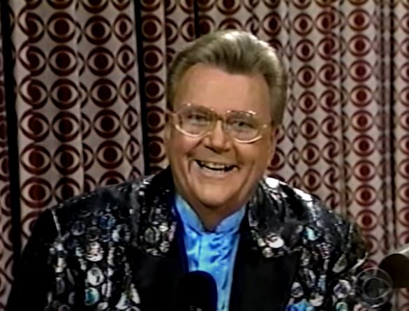 Rod is wearing a silver dotted & black jacket with black lapels and a blue collarless silk shirt