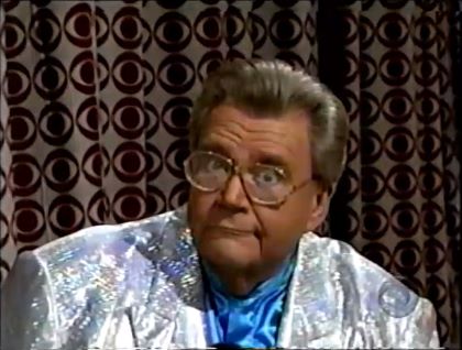 Rod is wearing a shiny silver jacket & light-blue collarless silk shirt