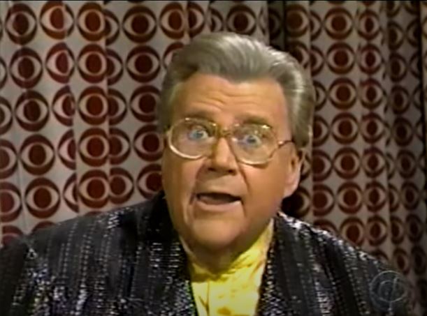 Rod is wearing a black shiny jacket & yellow silk collarless shirt