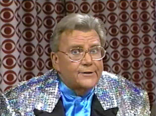 Rod is wearing a shiny silver jacket with black lapels & light blue collarless silk shirt