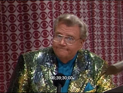 Rod is wearing a black-sequin over shiny-yellow jacket & a seafoam collarless silk shirt with matching pocket square