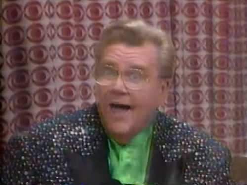 Rod is wearing a black jacket with shiny speckles & black lapels & a green collarless silk shirt