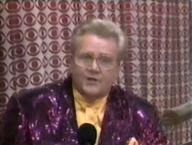 Rod is wearing a purple sequined jacket & mustard-yellow collarless silk shirt with matching pocket square